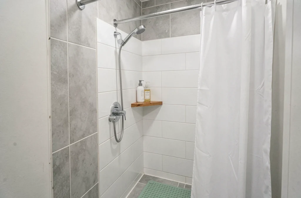 Coin douche rénové avec panneaux muraux blancs, pommeau chromé et étagère en teck, sans gros travaux