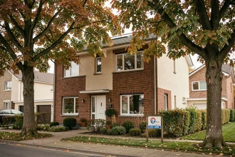 Maison à vendre en Seine-et-Marne avec panneau immobilier dans le jardin, façade en brique et enduit, entourée d'arbres aux feuilles automnales